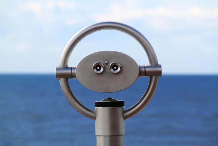 Coin-operated binoculars facing the ocean with a clear blue sky in the background.