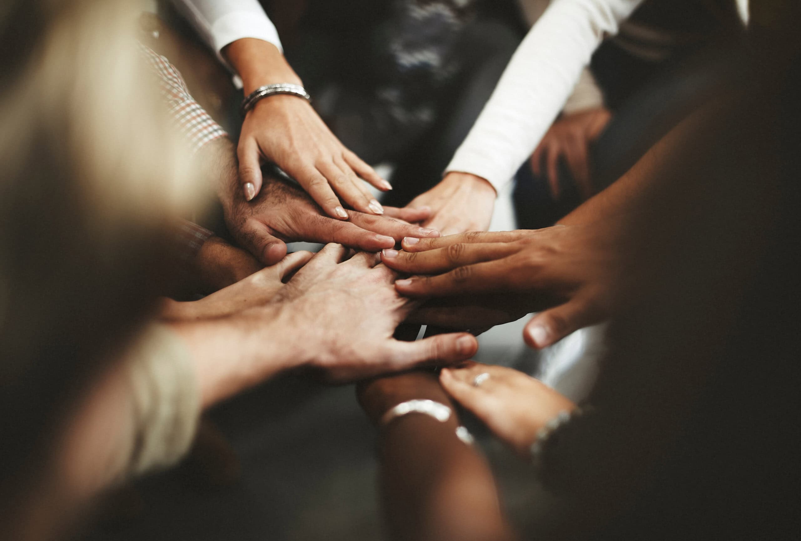 A diverse group of hands join together in the center of the image, symbolizing unity and teamwork, mirroring the collaborative spirit essential in a thriving market research platform.