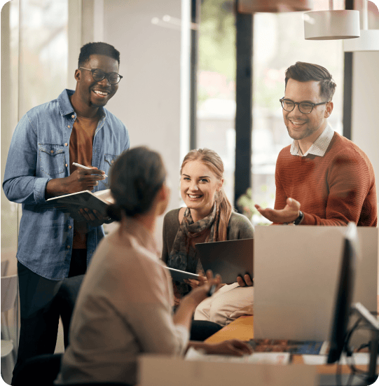 Four people engaged in a meeting; one woman, seated with a tablet loaded with insights from their market research platform, while three others stand, smiling and talking, in a bright office setting.