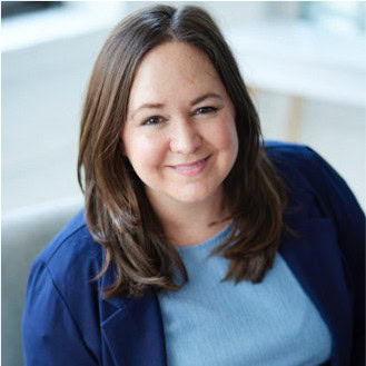 Sarah Tomasaiti with long brown hair wearing a blue shirt and dark blazer, smiling at the camera.