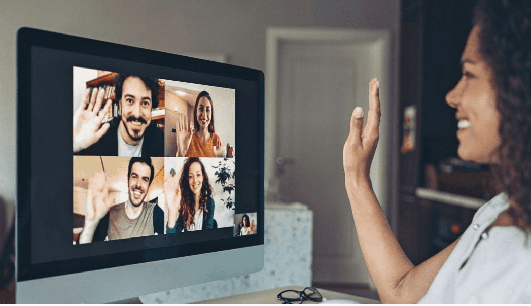 Person waving at four people on a computer screen during a video call.